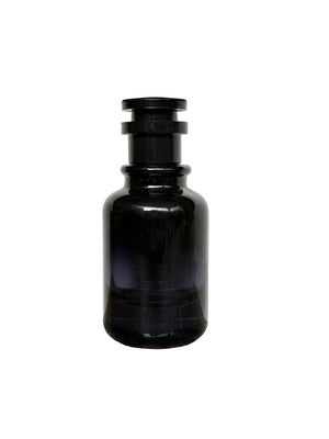 A dark amber glass bottle with a black screw cap, standing on a speckled granite countertop against a white wall.