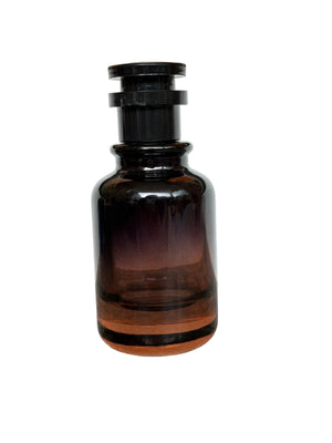 An amber glass dropper bottle with a black plastic cap, standing on a speckled granite countertop against a white wall.